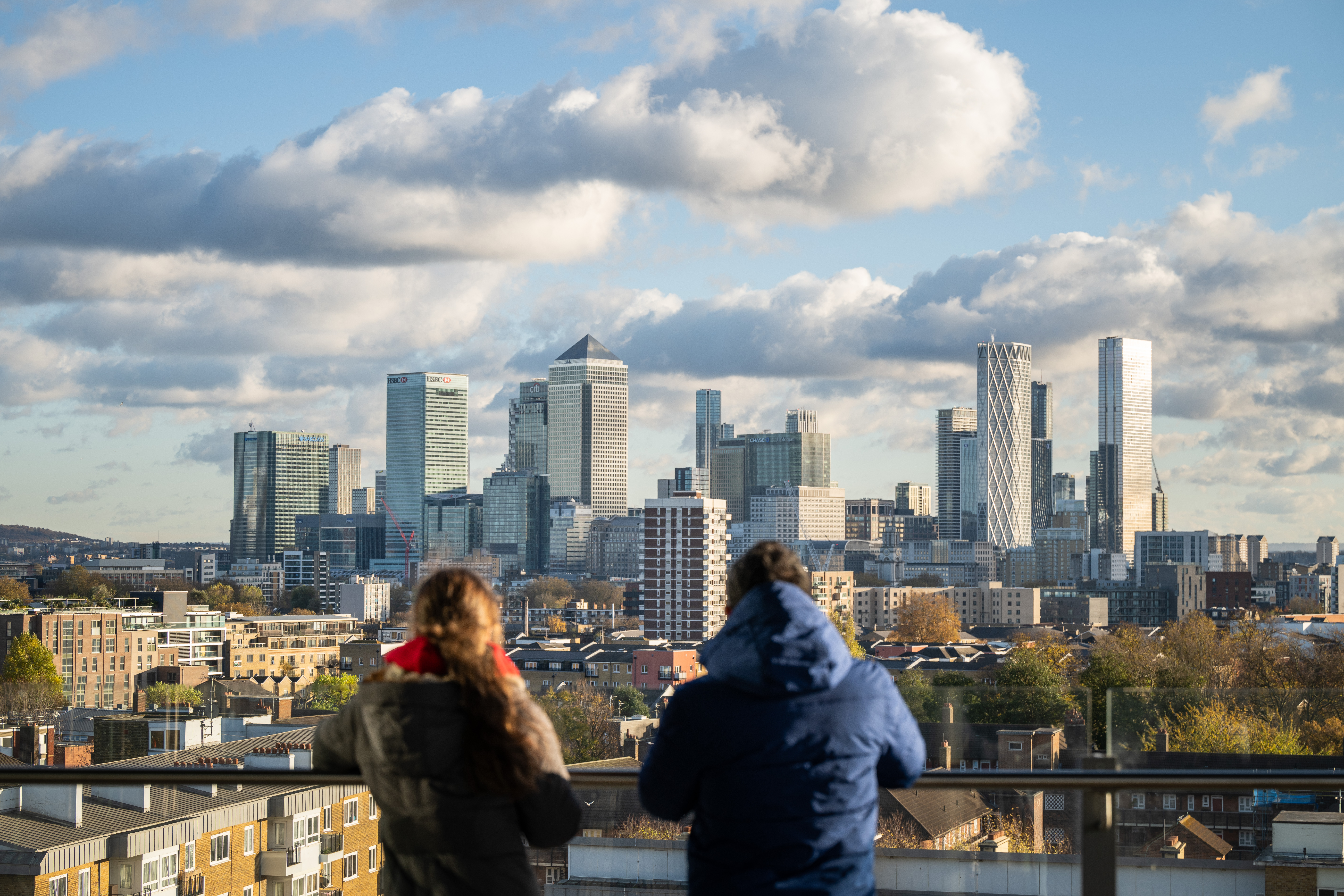Two students looking out at the Canary Wharf skyline from a Queen Mary rooftop on campus.