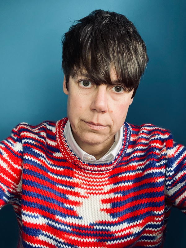 Isabel has short brown hair, brown eyes and wears a bold jumper in blue, red and white