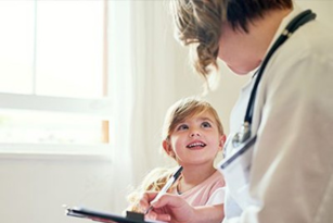 A little girl looking up at a doctor taking notes