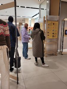 Two people have a discussion in the Dorcas Exhibition space. In the foreground are some mannequins with clothing on them.