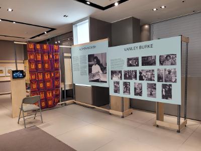 Two panels about Althea Mcnish and Vanley Burke with photographs from their lives. To the left if a quilt with a purple, magenta, and gold panel effect.