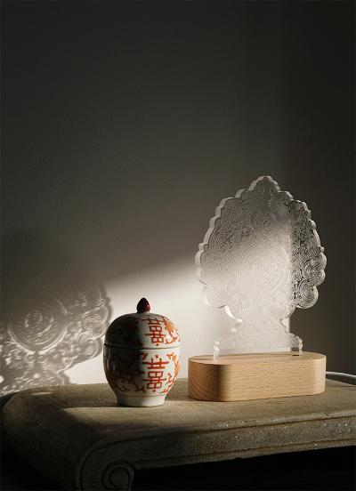 A glass ornament etched with a Miao paper design, next to some handmade pottery. The shadows behind the ornament show the same design.