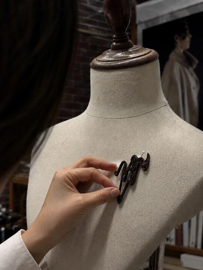 A person fixing a black broach to a mannequin bust.
