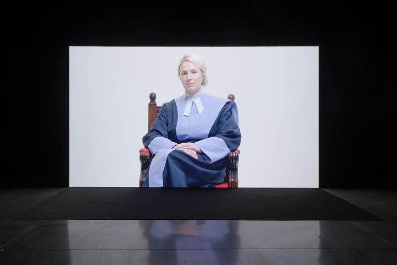 A blonde woman in a purple barristers outfit sitting on an antique chair.
