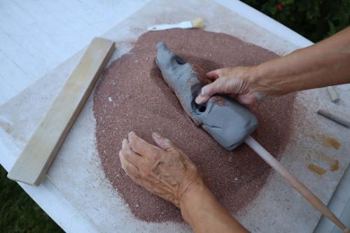 Someone putting molded clay into red toned sand.