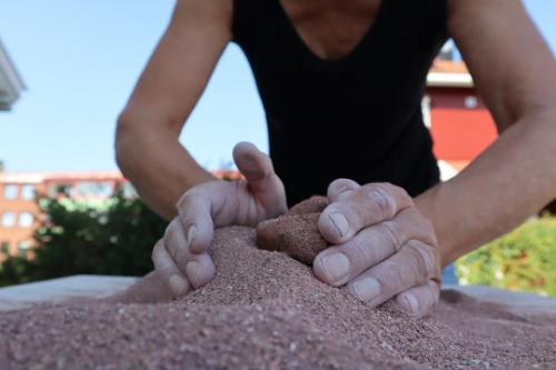 A person covering molded clay completely in red toned clay.