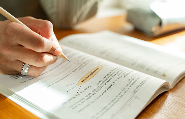Textbook open with hand holding a pen