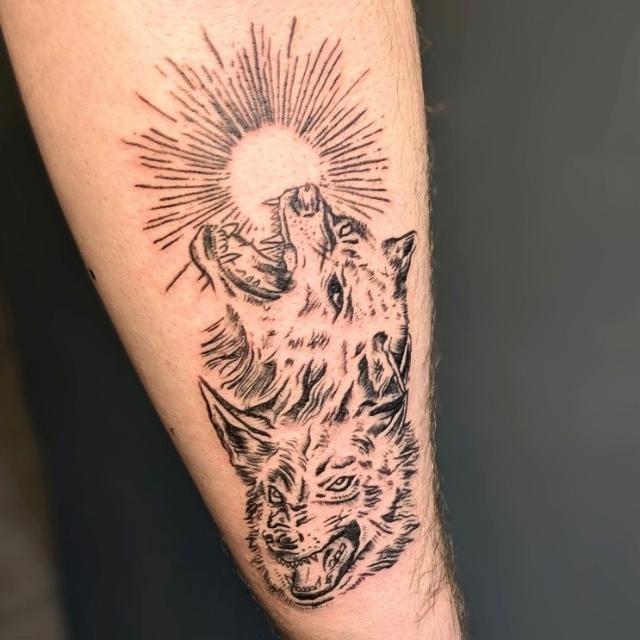 A tattoo of a two headed wolf. One is howling at a moon and the other is facing forward snarling.