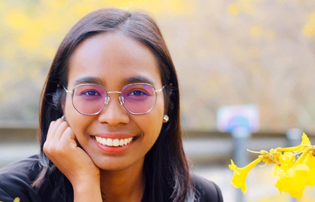 Nuanchan Changchit smiling, wearing glasses. Next to her is a yellow flower.