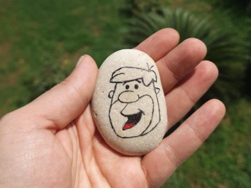A person holding a stone with a drawing of Fred Flinstone.