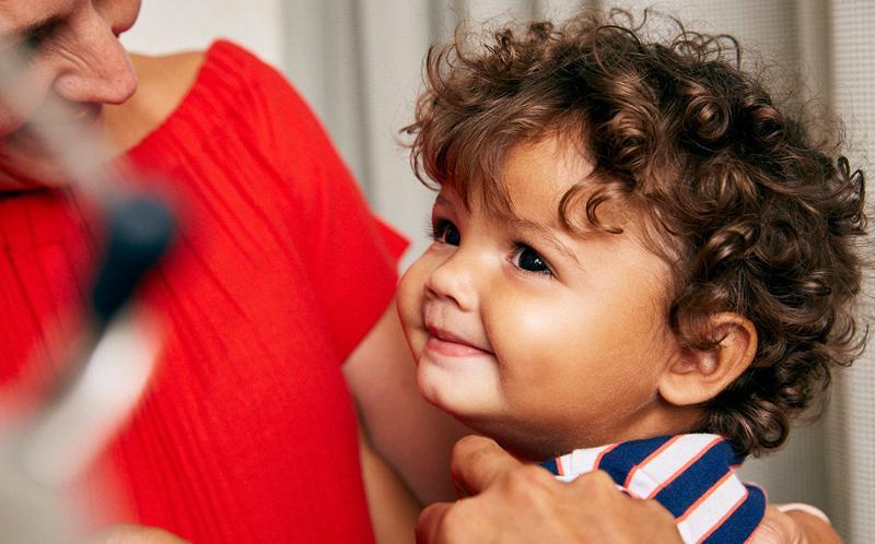 Toddler smiling and receiving a vaccine in his arm while sitting on a parent's knee