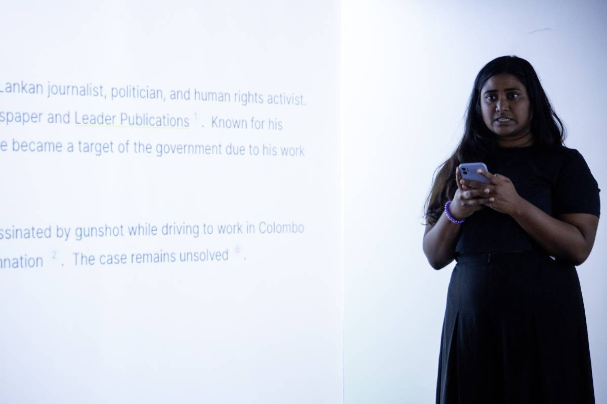 A woman stands in front of prokected text, performing a text which she is reading on her phone