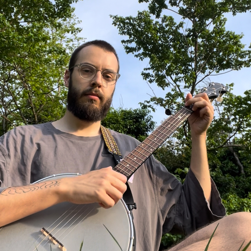 A Masters student playing guitar in a park looking at the camera