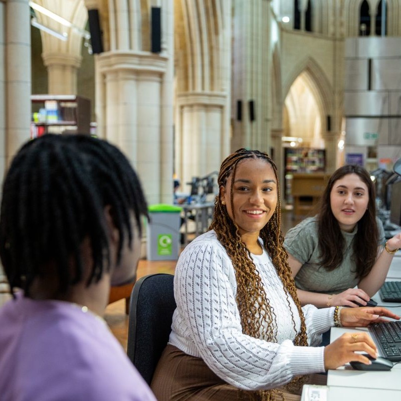 3 students in Whitechapel library sitting at desk and talking