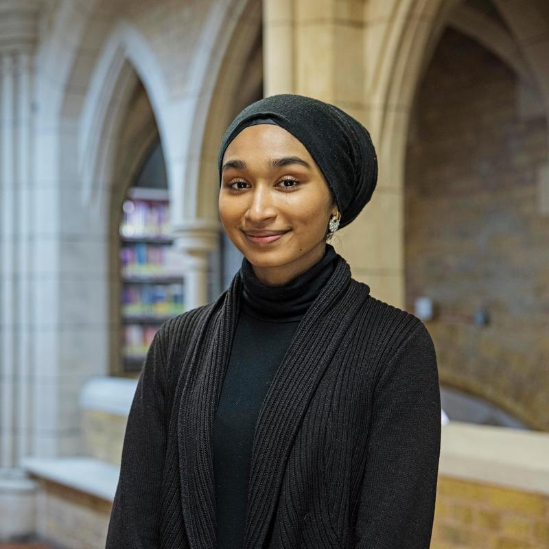 Smiling student inside a library, wearing a black top and jacket