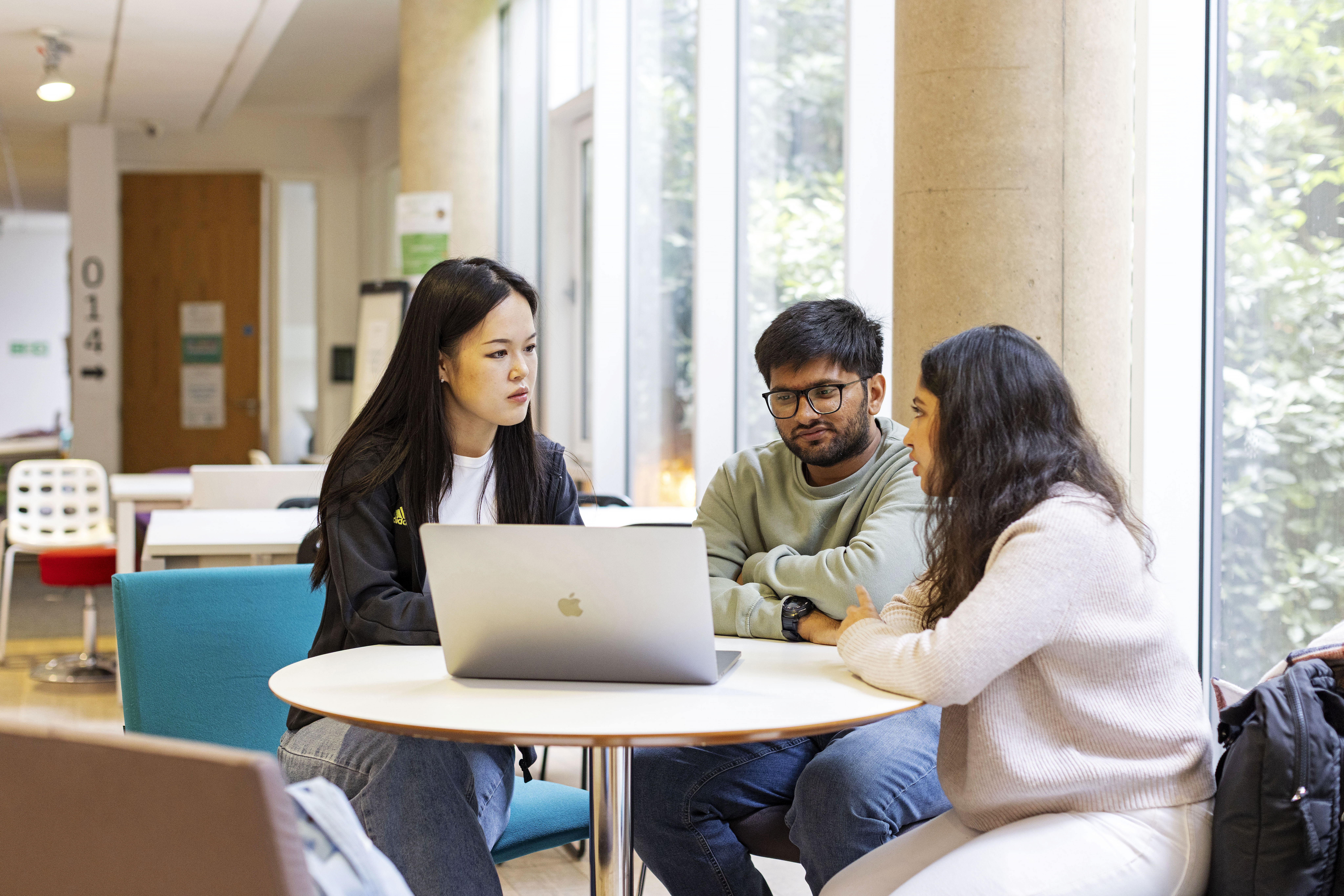 Three postgraduate students sitting at a desk together, a laptop is on the table