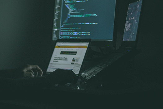 A person using a laptop and other screens with code on them