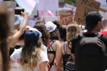 A group of women at a protest seen from behind. In the distance, ahead of them there are signs and placards.