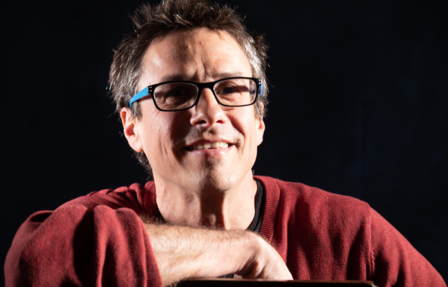 Neve Gordon smiling and wearing a red jumper.