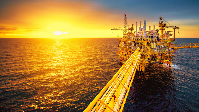 An oil rig in the ocean at sunset