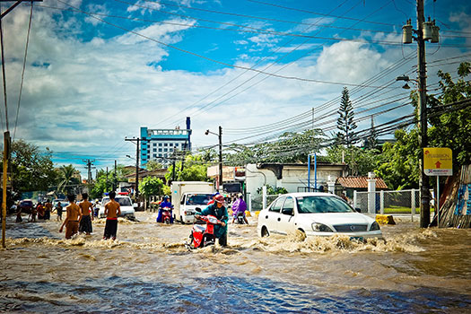 People walking and driving through a street flooded with water
