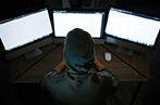 Person wearing a hoodie, with the hood up, looking at computer monitors.