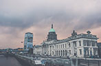 The Irish Houses of Parliament building. It is neo-classical in style, with columns at the front. There is a aged bronze done with a clock on top of the building.