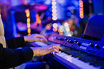 Musician pianist playing keyboard digital piano with blue blurred background with lights in concert.