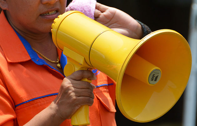 A person wearing an orange coat using a yellow megaphone. Their face is largely obscured.