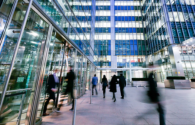 Commuters walking in and out of a London glass-fronted office building.