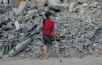 A Palestinian child standing in front of rubble in Gaza. She is missing her right leg and using crutches.