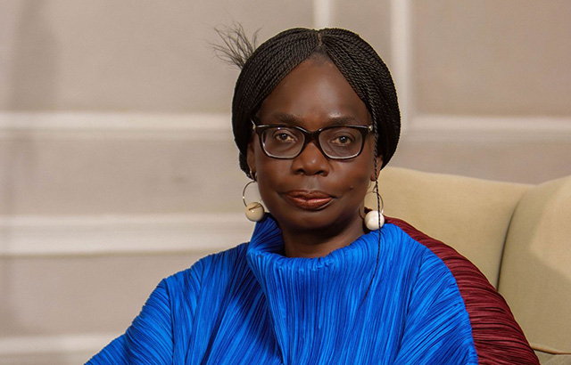 Phoebe Okowa sat on a cream chair wearing a blue and brown kaftan.