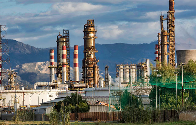 An oil refinery with various chimneys. There are mountains in the background.