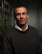 Professor Neve Gordon wearing a slate coloured jumper and shirt. He is standing in an archive.