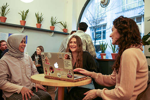 Queen Mary postgraduate law students sitting in a café with a laptop and having a discussion.