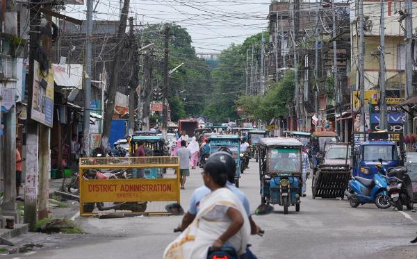 People riding a scooter through a street in Assam, India.