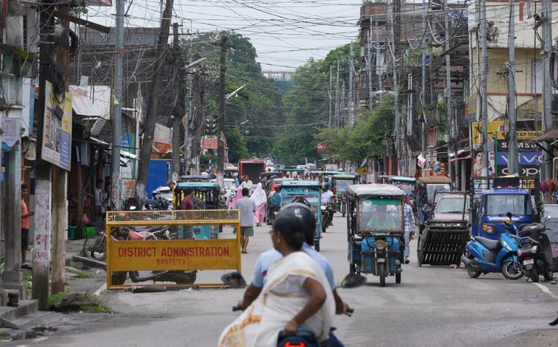 People riding a scooter through a street in Assam, India.