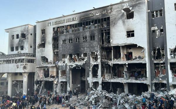 A partially bombed hospital building in Gaza. People are gathered outside by the rubble.