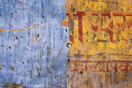 A weathered blue and yellow wall covered in graffiti written in Devanagari script.