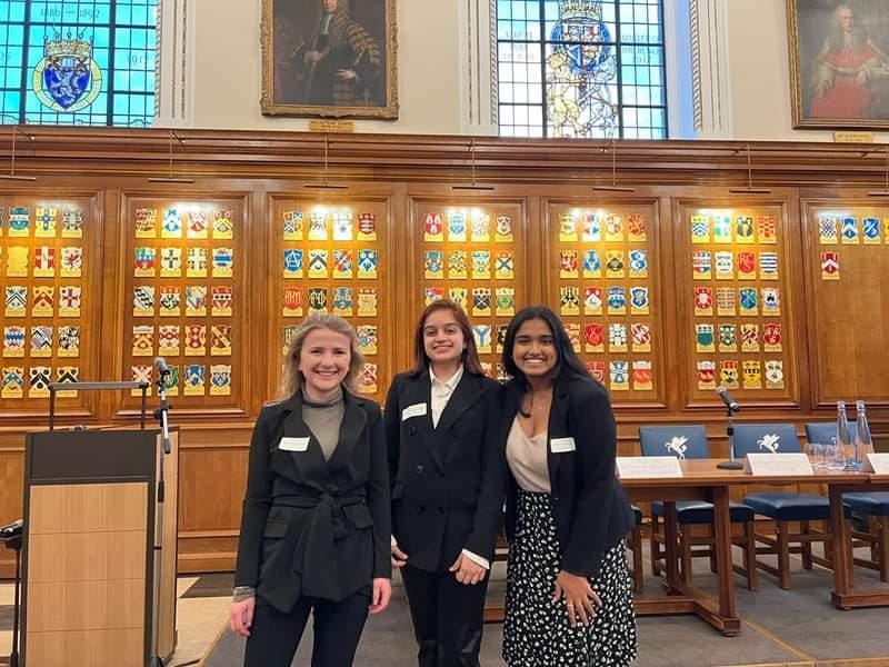 Three students standing in front of beautiful old bookshelves in the library
