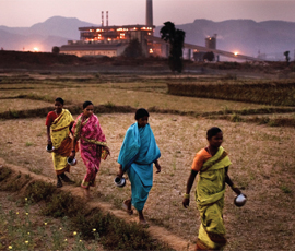Indian women walking through a field in front of a factory