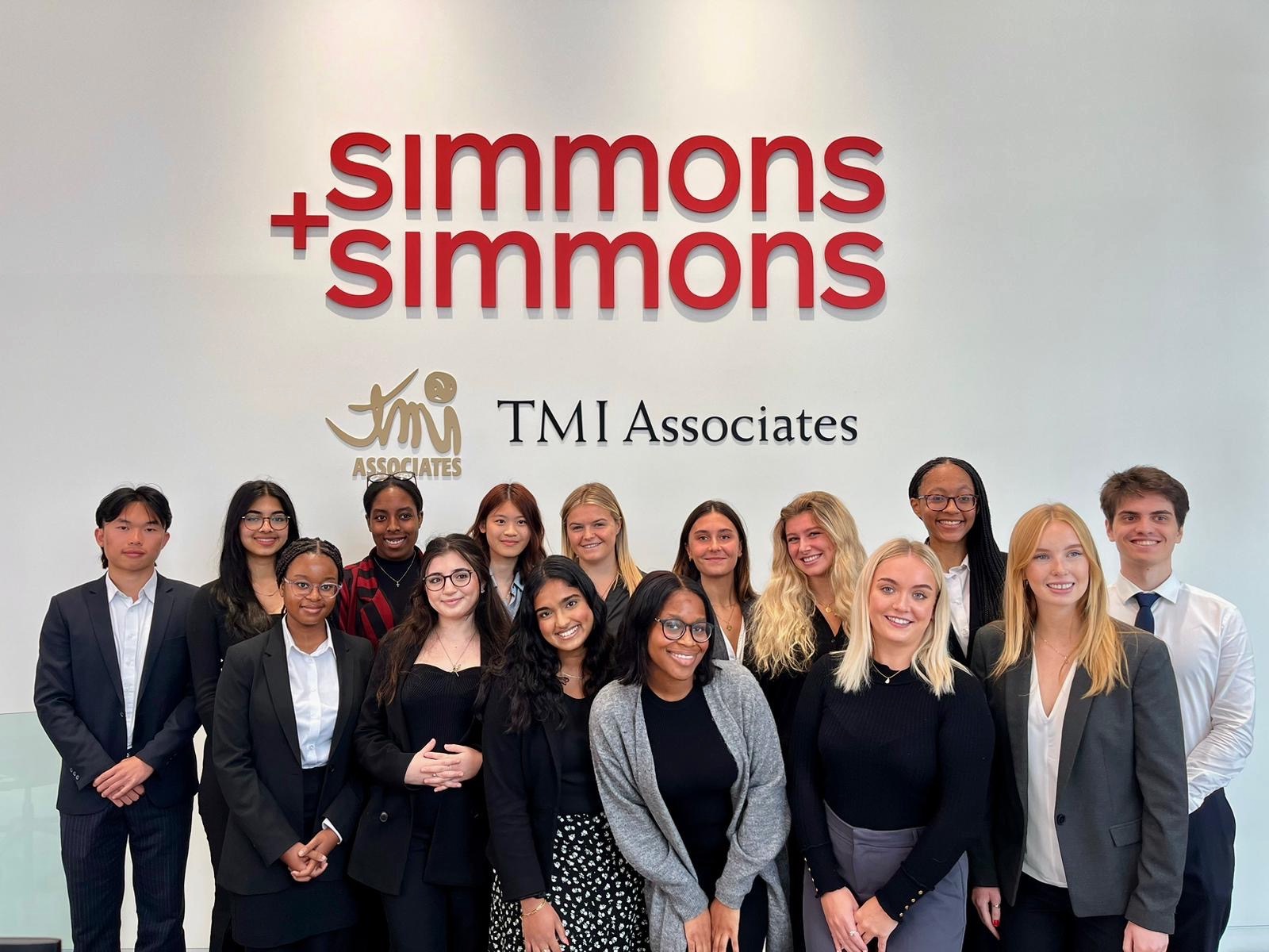 A group of students standing in front of a sign which says 'simmons + simmons'