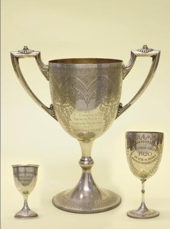 Photograph of a set of three silver trophies, one large one in the centre with two smaller trophies, one each side of the largest