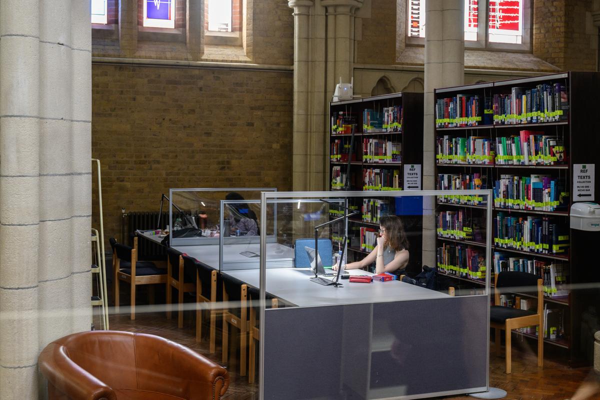 Student sat at group of study desks in front of bookshelf at Whitechapel Library