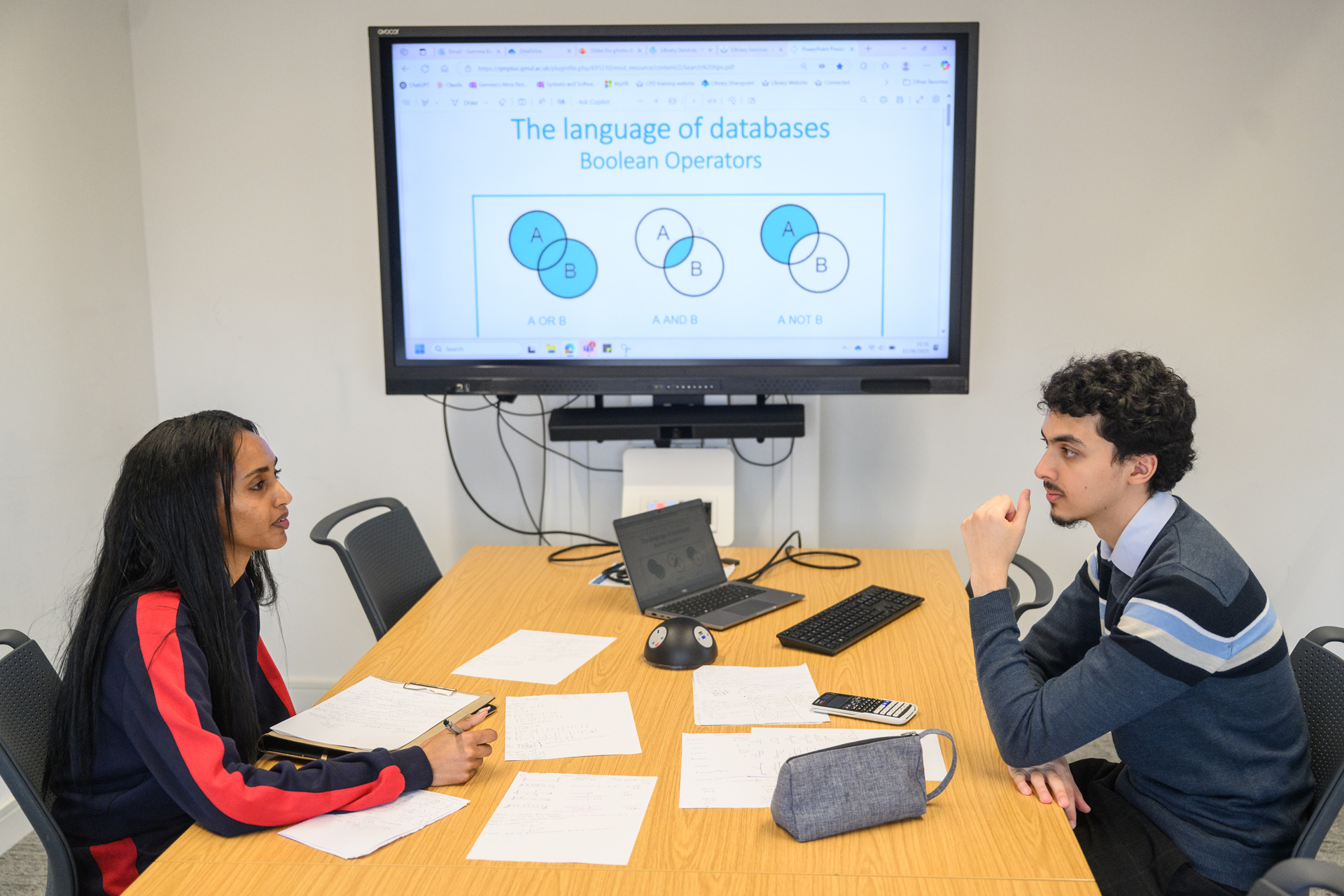Students using group study room with notes on desk and laptop connected to screen