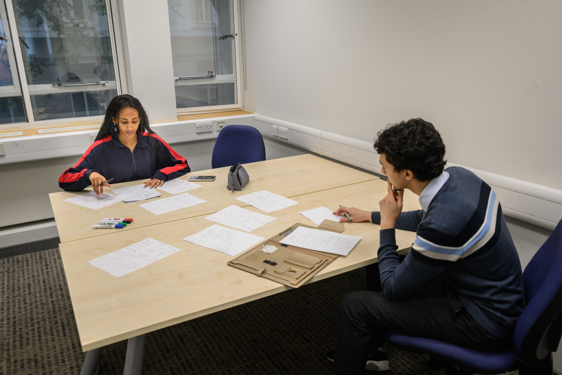 Two students working collaboratively in a group study room sharing notes