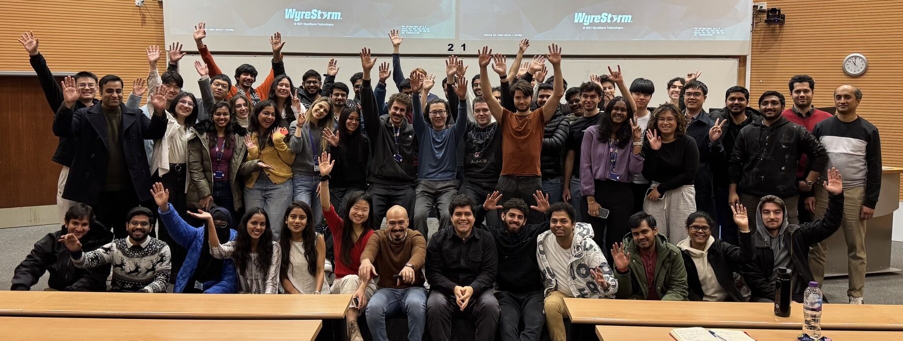 Group of students next to lecturer looking at camera and waving