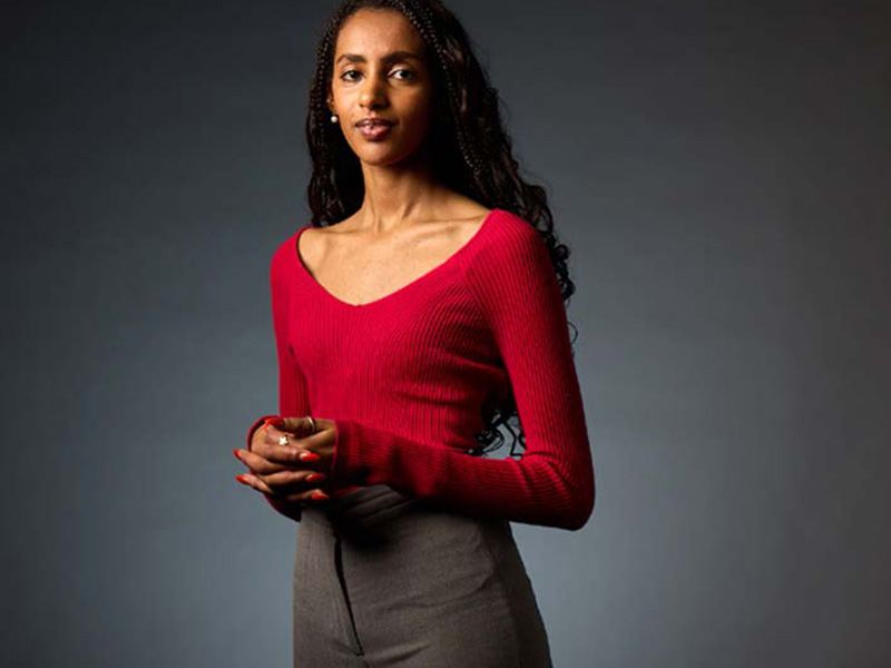 Fasika wearing a long sleeved red top in front of a grey background