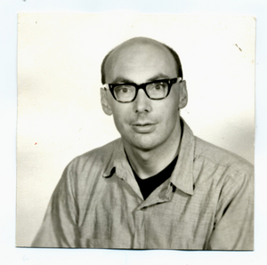 A vintage black‑and‑white portrait of a person seated and facing forward, wearing a collared shirt over a dark top against a plain light background.