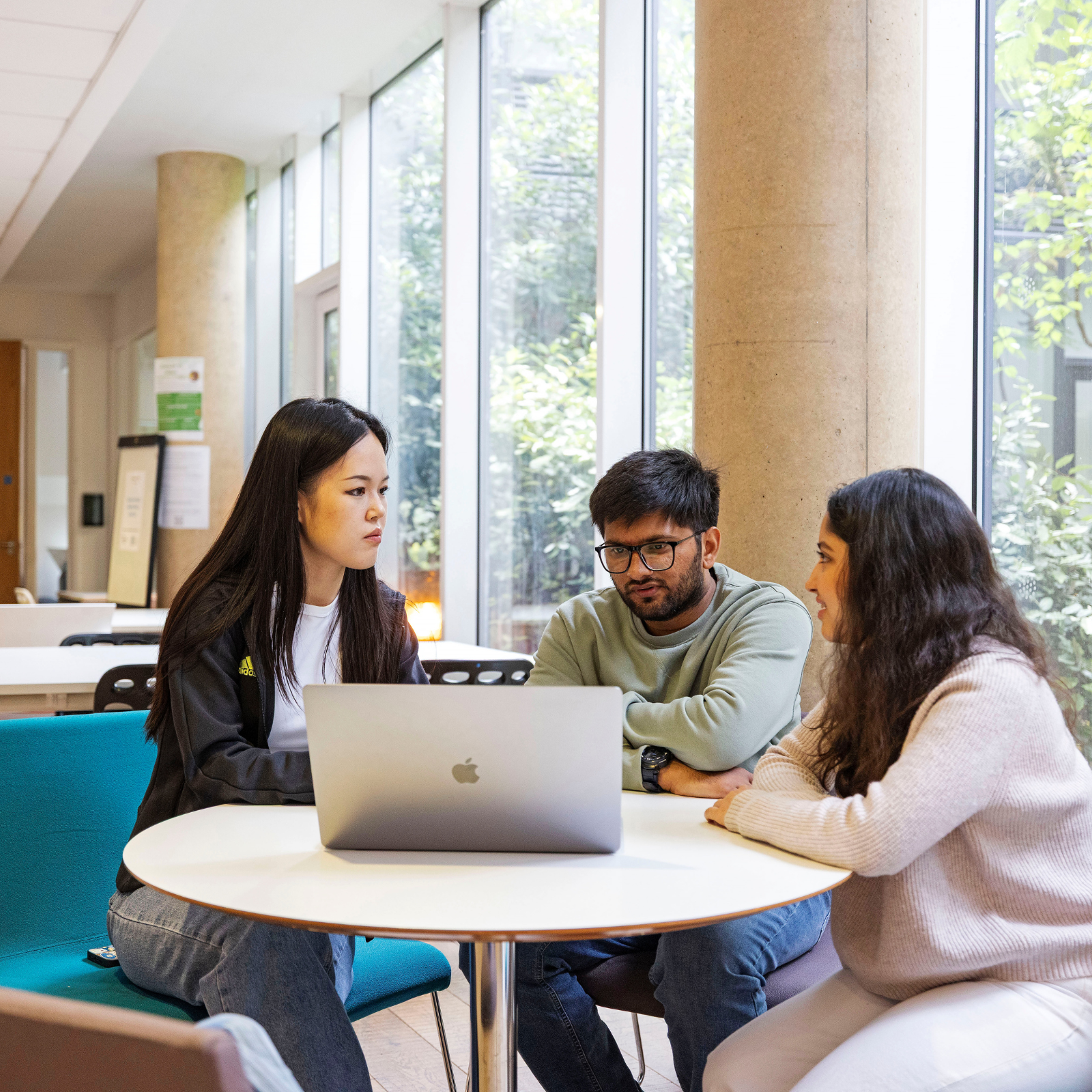 Three students are sitting around a laptop